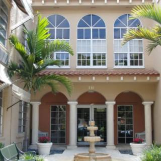 A Mediterranean-style building with large arched windows, palm trees, and a central fountain.