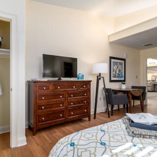 A cozy bedroom with a dresser, TV, and work desk.