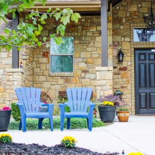A cozy front porch with two blue chairs, potted plants, and a stone wall entrance.