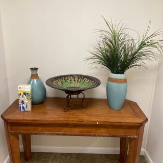 A wooden table decorated with vases, a plant, and a decorative bowl in a corner setting.