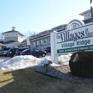 A housing complex with a sign that reads 'The Villages Village Ridge' on a snowy day.