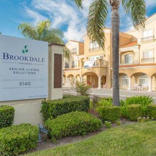 A residential building with a prominent sign and well-maintained landscaping, featuring palm trees on a sunny day.