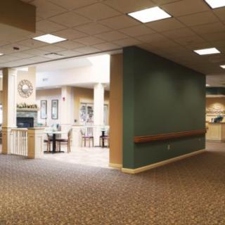 A spacious hallway with a carpeted floor and bright lighting, leading to a seating area.
