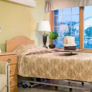 A cozy bedroom with a hospital bed next to a nightstand, featuring a lamp and a window view.