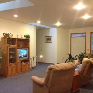 A cozy living room with recliner chairs facing a TV and an entertainment center, accented by indoor plants.