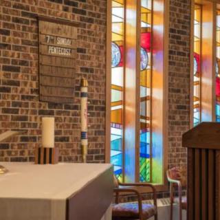 Interior of a church featuring stained glass windows, an altar, candles, and a pulpit.