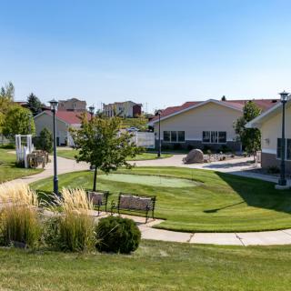A peaceful residential area with well-maintained lawns, benches, and a winding pathway.