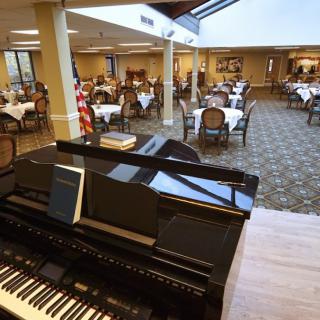 A spacious dining area with elegant tables and a grand piano in the foreground.