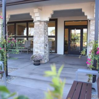 A welcoming building entrance with stone pillars and outdoor seating, surrounded by plants and flowers.