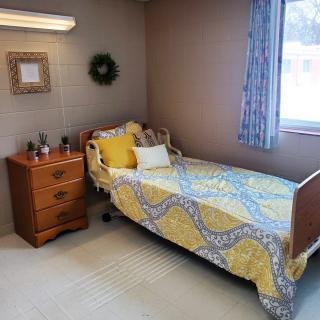 A cozy bedroom with a single bed featuring yellow bedding, next to a wooden nightstand and a window with curtains.