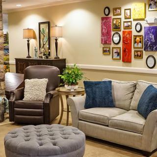 A cozy living room with a sofa, armchair, ottoman, and colorful wall art.