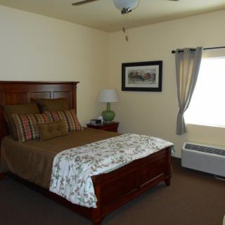 A cozy bedroom with a wooden bed frame, decorative bedding, a bedside lamp, and a window with curtains.