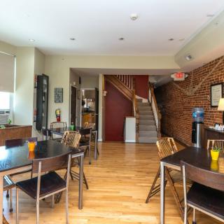 A cozy dining area with multiple tables and chairs, featuring a wooden floor and exposed brick walls.