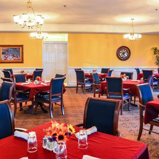 A spacious restaurant dining room with red tablecloths and elegant lighting.