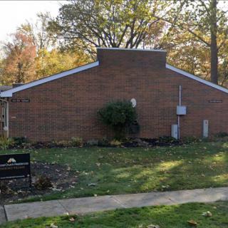 A brick building with a surrounding lawn and autumn trees, featuring a bench on a pathway.
