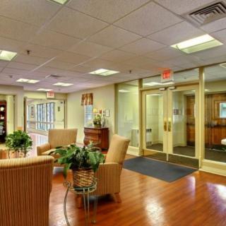 A well-lit lobby area with comfortable seating and plants, featuring glass doors and wooden floors.