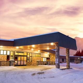A building illuminated by lights sits in a snowy landscape at sunset.