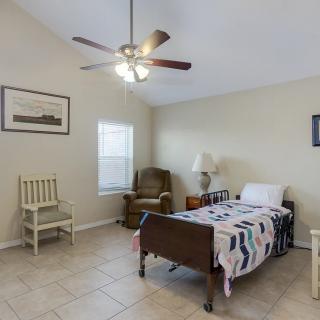 A cozy bedroom with a single bed, two chairs, a ceiling fan, and a lamp.