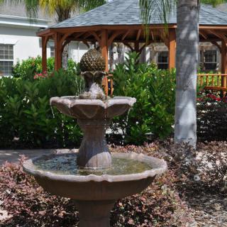 A tranquil garden setting featuring a tiered fountain and a wooden gazebo surrounded by lush greenery.
