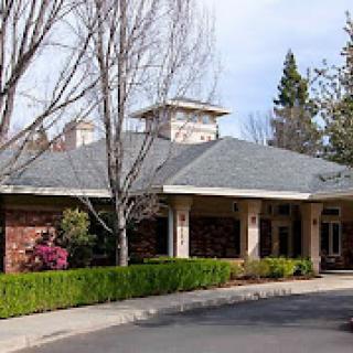 A one-story residential building surrounded by trees and shrubs.
