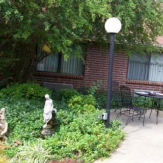 A tranquil garden space featuring a statue, lamp post, and outdoor seating next to a brick building.