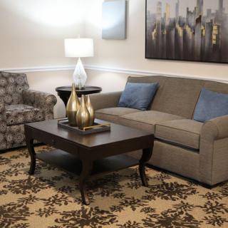 A cozy living room with a sofa and armchair arranged around a wooden coffee table, adorned with decorative items and illuminated by a modern lamp.