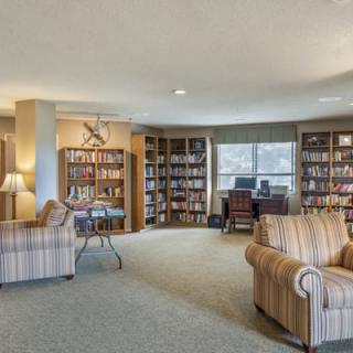 A cozy library with bookshelves, armchairs, and a reading area near a window.