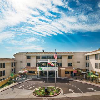 A hotel building with a circular driveway and flags at the entrance against a blue sky.