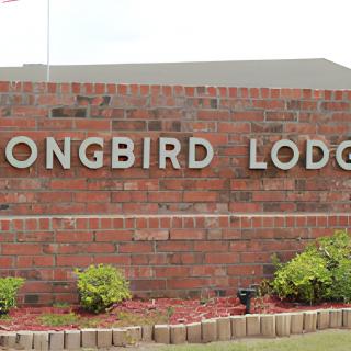 A brick wall sign for 'Songbird Lodge' with landscaping at the base.