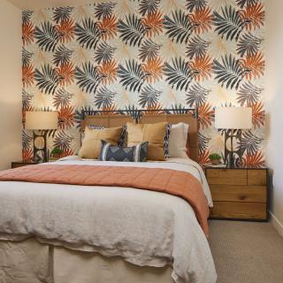A stylish bedroom with vibrant floral wallpaper, a neatly made bed, and matching bedside lamps.