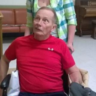 A person in a red shirt is seated in a wheelchair indoors.