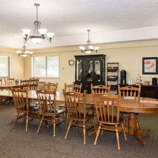 A spacious dining room featuring a large wooden table surrounded by matching chairs, with elegant lighting fixtures overhead.