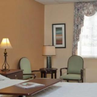 A cozy hotel room featuring a bed, two lamps, chairs, and a window with curtains.