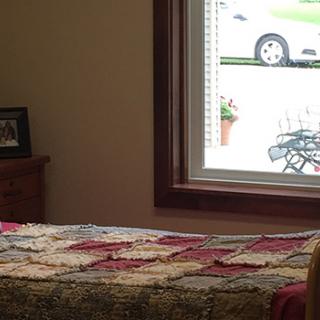 A cozy bedroom with a quilted bedspread and a view of the outdoors through the window.