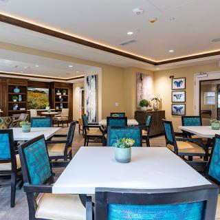 A modern indoor dining room with neatly arranged tables and chairs, featuring decorative plants and artwork.