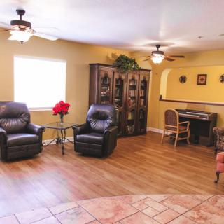 A cozy living room featuring recliner chairs, a wooden bookshelf, a small desk, and ceiling fans.