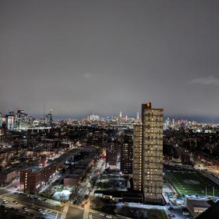A panoramic view of a city skyline illuminated at night, showcasing urban architecture against a cloudy sky.