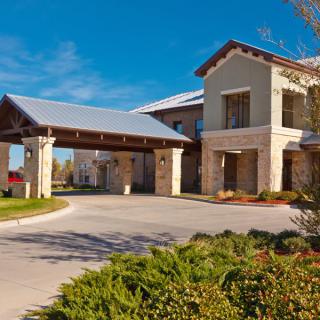 A modern building with a covered entrance and landscaped surroundings under a clear blue sky.