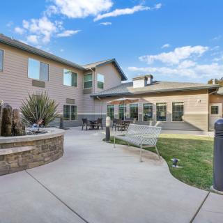 A residential building with an outdoor courtyard and landscaped garden area under a blue sky with clouds.