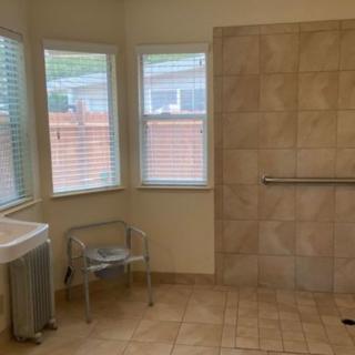 A spacious bathroom with a tiled shower area, grab bar, and windows allowing natural light.