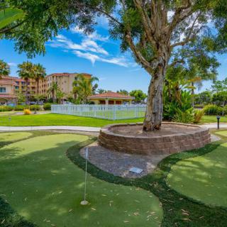 A serene mini golf course surrounded by lush greenery and a resort in the background.