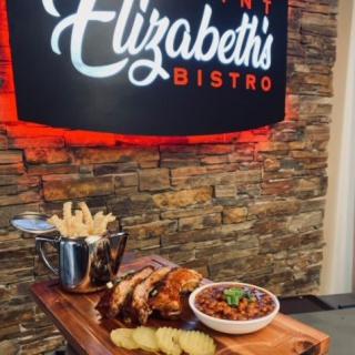 A delicious meal at Elizabeth's Bistro featuring fries, a meat dish, and beans served on a wooden platter.