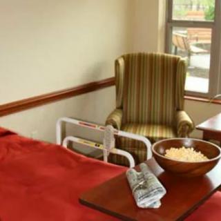 A hospital room with a bed, a comfortable chair by the window, and a bowl on a tray.