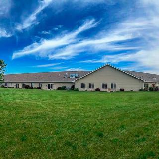 A wide, single-story building surrounded by a grassy lawn under a blue sky with wispy clouds.
