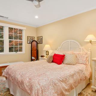 A cozy bedroom with a bed adorned with pink bedding, nightstands with lamps, and a mirror next to a window.