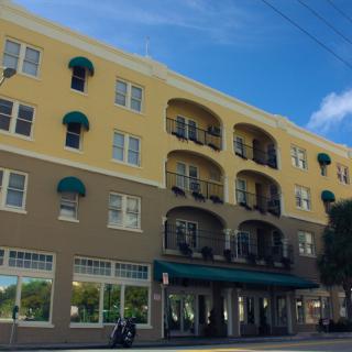 A multi-story residential building with yellow and brown facade, featuring balconies and storefronts at the ground level.