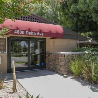 Entrance of a building with red awning and address '4800 Delta Ave', surrounded by landscaping.