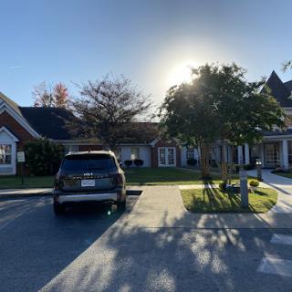 A sunny day outside a residential building, featuring a parked car and trees.