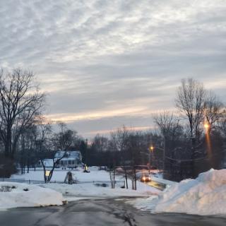 A serene winter evening scene with snowy ground and a cloudy sky.