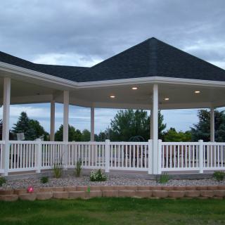 A large gazebo with a dark roof and white railings set in a garden area.